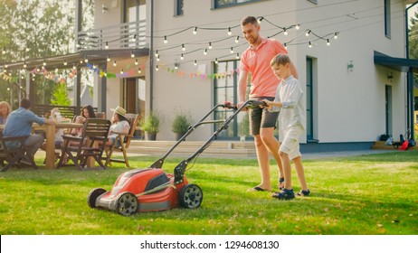 Good Father Teaches Son How to Use Walk Behind Lawn Mower, They Push it Together, Cutting Grass. Family Spending Time Together on a Sunny Day.
