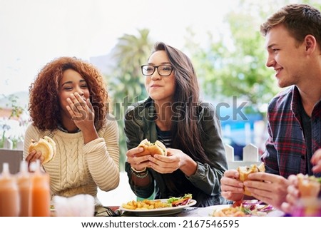 Good food and laughter go hand-in-hand. Cropped shot of three friends eating burgers outdoors.