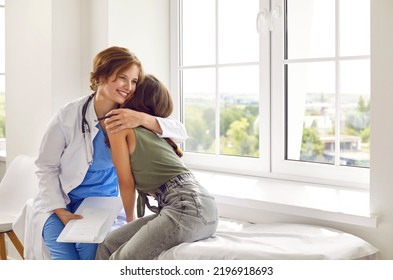 Good, Friendly Doctor Supporting Her Teenage Patient During Health Checkup. Happy, Smiling Female Pediatrician Hugs Teen Child Girl While Sitting On Examination Bed By Window In Light Medical Office