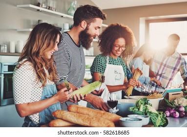 Good friends laughing and talking while preparing meals at table full of vegetables and pasta ready for cooking in kitchen