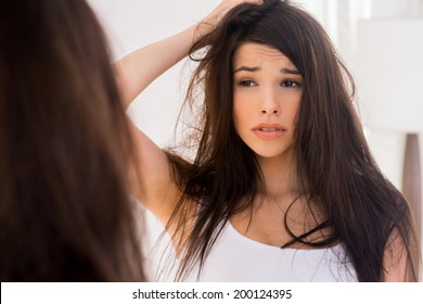 Good Morning? Frustrated Young Woman Looking At Her Reflection In The Mirror And Holding Hand In Hair