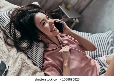 So Good To Hear You! Top View Of Attractive Young Woman Talking On Her Smart Phone And Smiling While Lying On The Bed At Home