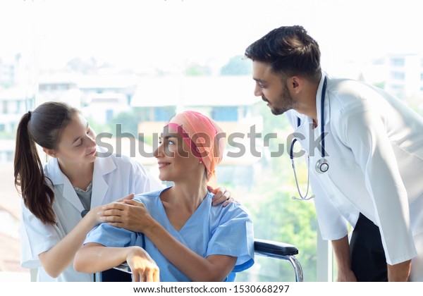 Good hospital provide quality medical service.\
Professional doctor, nurse take care a patient.  Senior Caucasian\
woman cover head with a cloth caused of chemotherapy cancer,\
smiling sitting wheelchair