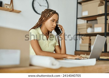 good looking african american woman talking by phone while working at her laptop, delivery concept