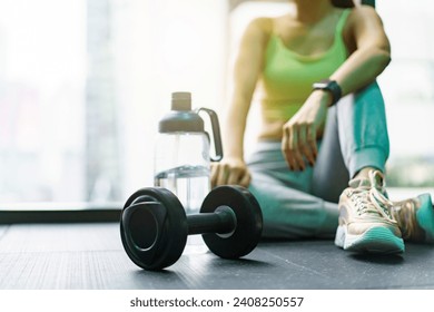 Good looking - beautiful Asian woman relaxing in the gym after made weight training and cardio workout, woman sitting or resting on the bench while drinking water after exercise. - Powered by Shutterstock