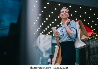 Good Looking Caucasian Customer Holding Mobile Standing Near Mall Doing Shopping In Black Friday, Cheerful Caucasian Customer With Paper Bags Using Public Internet Connection On Smartphone Gadget