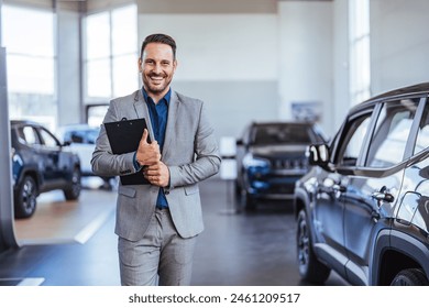 Good looking, cheerful and friendly salesman poses in a car salon or showroom and looks at camera. Successful businessman in a car dealership - sale of vehicles to customers - Powered by Shutterstock