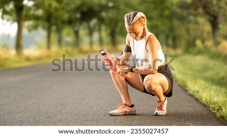 Good looking female athlete checking her heart rate on smart watch, holding water bottle for hydration, while resting.