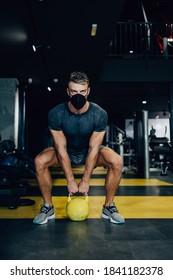 Good Looking Handsome Male Athlete With Protective Face Mask Exercising In Modern Fitness Gym. Dark Muddy Light With Strong Shadows. Pandemic Sports Indoors Concept.