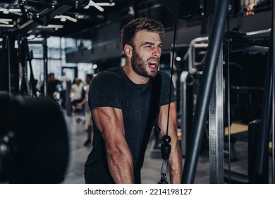 Good Looking Handsome Male Athlete Exercising In Modern Fitness Gym. Dark Muddy Light With Strong Shadows. Indoors Sport Concept.