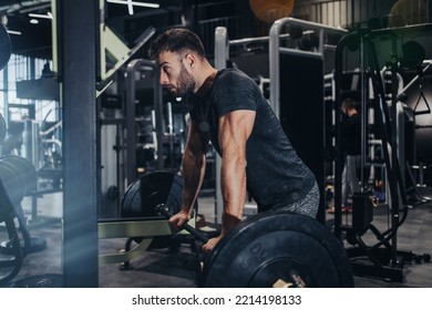 Good Looking Handsome Male Athlete Exercising In Modern Fitness Gym. Dark Muddy Light With Strong Shadows. Indoors Sport Concept.