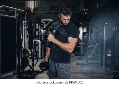 Good Looking Handsome Male Athlete Exercising In Modern Fitness Gym. Dark Muddy Light With Strong Shadows. Indoors Sport Concept.