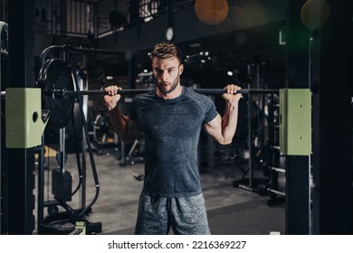 Good Looking Handsome Male Athlete Exercising In Modern Fitness Gym. Dark Muddy Light With Strong Shadows. Indoors Sport Concept.