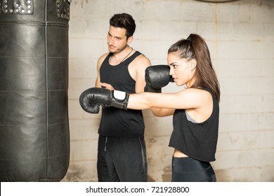 Good looking Hispanic woman training in front of a punching bag during a boxing class in a gym - Powered by Shutterstock