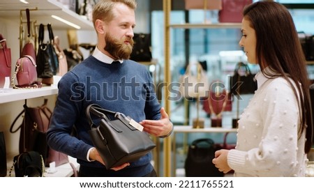 Good looking man customer try to choose a bag from the accessories store while a beautiful saleswoman try to explain some information about the product