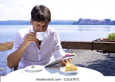 Good looking man drinking cappuccino in front of lake working with electronic tablet