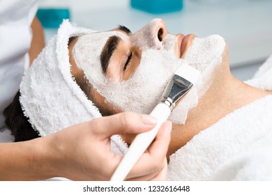 Good looking man receiving facial mask with rejuvenating effects in spa beauty salon.