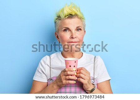 good looking mature woman tasting juice, close up portrait. isolated blue background. pleasant taste , stylish woman has coffee break.
