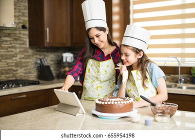 Good Looking Mother And Daughter Decorating A Cake And Looking At An Online Tutorial On A Tablet