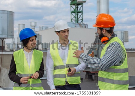 Good looking multiethnic group of workers in a modern building construction site analyzing the plan of construction they wearing the safety helmets