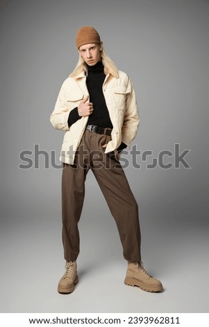 good looking non binary model in trendy beanie hat posing with one hand in pocket, fashion concept
