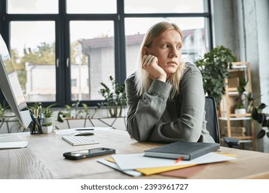 good looking non binary person in casual attire sitting at table with hand under chin, business