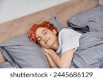 good looking red haired queer person in cozy homewear napping in her bed at home, leisure time