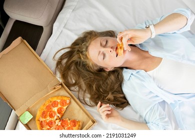 Good looking redhead woman in her 30s  enjoining eating pizza and closes her ises. Top view. The concept of quick snacks, lazy food, delivery. - Shutterstock ID 2191031249