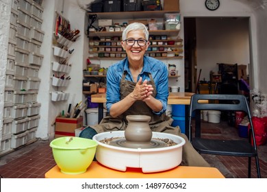 Good looking senior female potter working on pottery wheel while sitting  in her workshop - Powered by Shutterstock