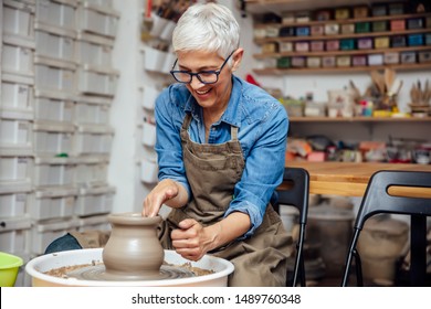 Good looking senior female potter working on pottery wheel while sitting  in her workshop