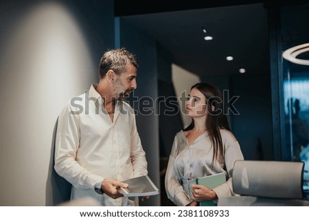 Good looking, senior, male employee flirting with his younger female colleague during work at modern office.