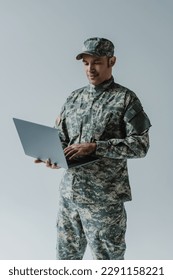 buen aspecto de soldado con uniforme del ejército y gorra usando laptop aislada en gris