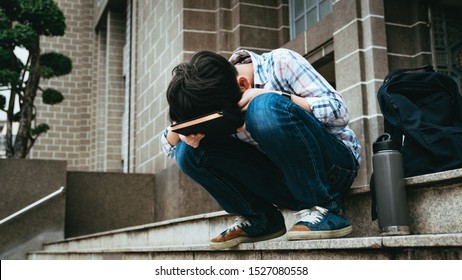 Good Looking Teenage Asian Boy Sit On Stairway In Front Of High School Building, Bend His Face Down On Notebook, Frustrated, Overwhelmed As He Struggle For Exam Preparation, Heavy Homework, Workload.