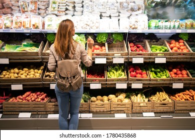 Good looking woman standing in front of vegetable shelves choosing what to buy. Buying groceries and healthy organic food in supermarket. - Powered by Shutterstock