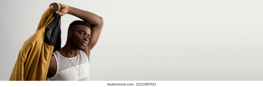 Good looking young african american man in sleeveless t-shirt wearing bomber jacket and standing isolated on grey, contemporary shoot featuring stylish attire, banner, muscular, fashion statement