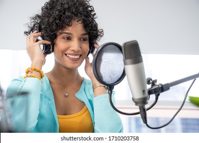 Good Looking Young Black Female Making An Online Podcast Recording For Her Online Show. Attractive Millennial African American Business Woman Using Headphones Front Of Microphone For A Radio Program.