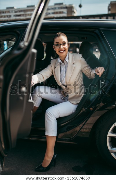 Good looking young business woman sitting on\
backseat in luxury car. She smiling and looking out. Transportation\
in corporate business\
concept.