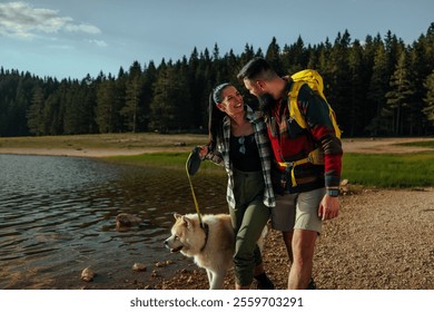 Good looking young couple in hiking gear by a lake in the wilderness with a dog on a a leash, smiling and enjoying a beautiful day outdoors. - Powered by Shutterstock