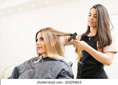 Good looking young hairstylist using a hair straightener on a woman's hair in a salon