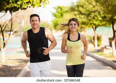 Good Looking Young Hispanic Couple Jogging Together At A Park On A Sunny Day And Smiling