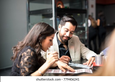 Good Looking Young Latin Couple Playing Bingo At A Casino And Having Fun