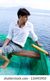Good looking young man posing serious  on a wood boat on a lake