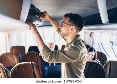 Good Looking Young Man Putting Hand Luggage In The Top Shelf In The Bus.
