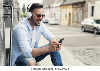 Good looking young man smiling and listening music on the street