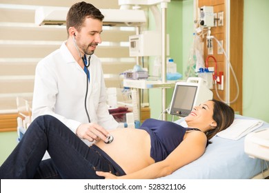 Good looking young obgyn examining a pregnant patient with an stethoscope in a hospital bed