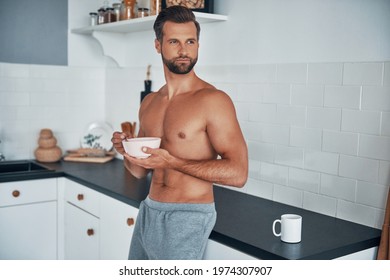 Good looking young shirtless man having breakfast while standing at home kitchen