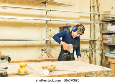 Good Looking Young Woman Working In A Woodshop And Using A Screwdriver