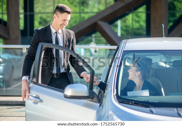 Good manners. Man standing\
near the open door of a car, a woman sitting inside, holding hands\
smiling