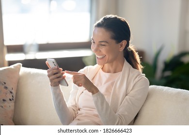 In a good mood. Laughing millennial woman taking cute selfie on couch at home on mobile phone webcam, having funny video conversation by video link, watching joyful photos or clips online using wifi