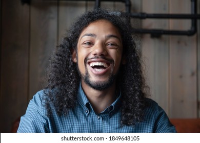 In a good mood. Profile picture of joyful laughing young mixed race male looking at camera, portrait of millennial biracial student sitting in cafe having fun with friends online using gadget webcam